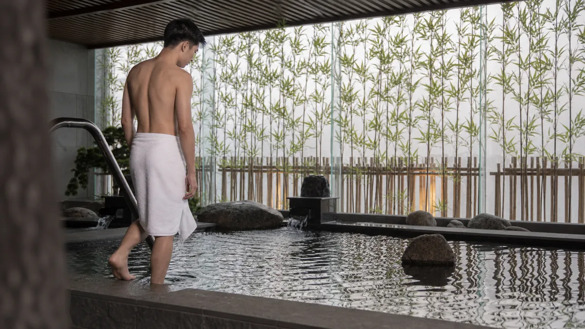Khách nam quấn khăn thử nước ở mép bể Onsen tại AMARE